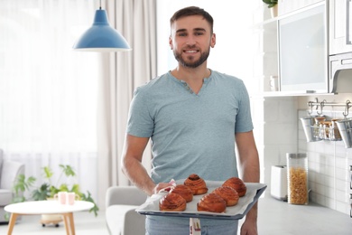 Photo of Young man holding tray of freshly oven baked buns in kitchen
