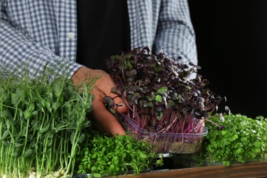 Photo of Man with different fresh microgreens on black background, closeup