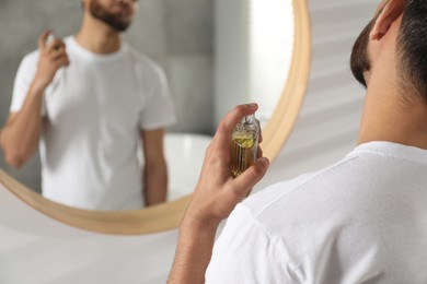 Photo of Man spraying luxury perfume near mirror indoors, closeup