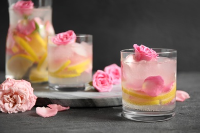 Delicious refreshing drink with lemon and roses on grey table