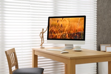 Modern PC on table near window with blinds in room