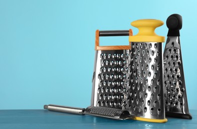 Photo of Different modern graters on light blue wooden table. Space for text