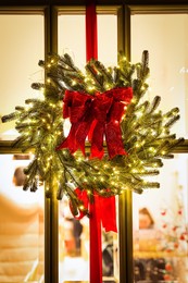 Photo of Beautiful Christmas wreath with ribbons and festive lights hanging on door
