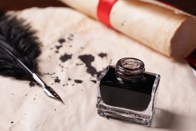 Photo of Open inkwell and feather pen on vintage parchment with stains, closeup