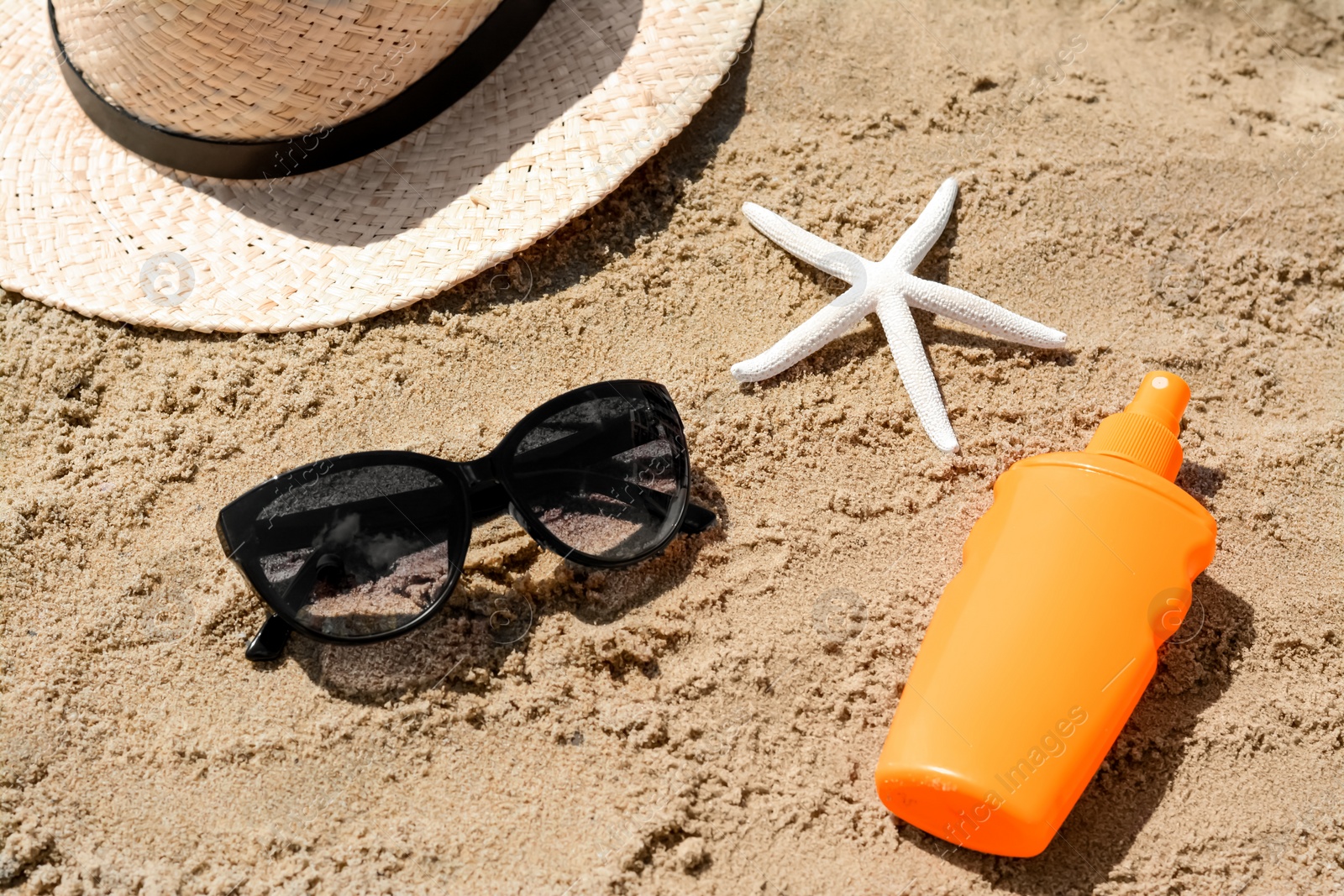 Photo of Blank bottle of sunscreen, starfish and beach accessories on sand