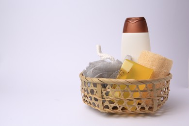 Photo of Wicker basket with shower puff, loofah sponge and cosmetic products on white background, space for text