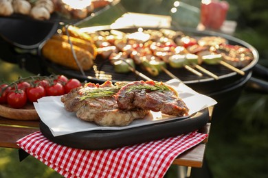 Photo of Tasty cooked meat and cherry tomatoes on table near barbecue grill outdoors