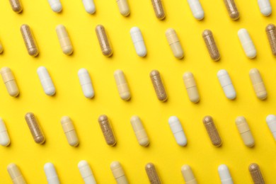Photo of Different vitamin capsules on yellow background, flat lay