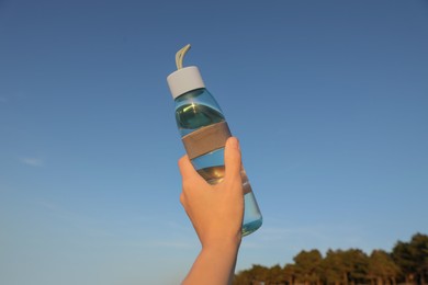 Photo of Woman holding glass bottle with water against blue sky, closeup