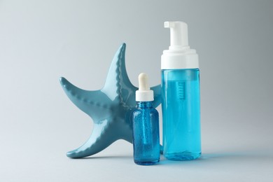 Photo of Bottles of cosmetic products and decorative starfish on light grey background