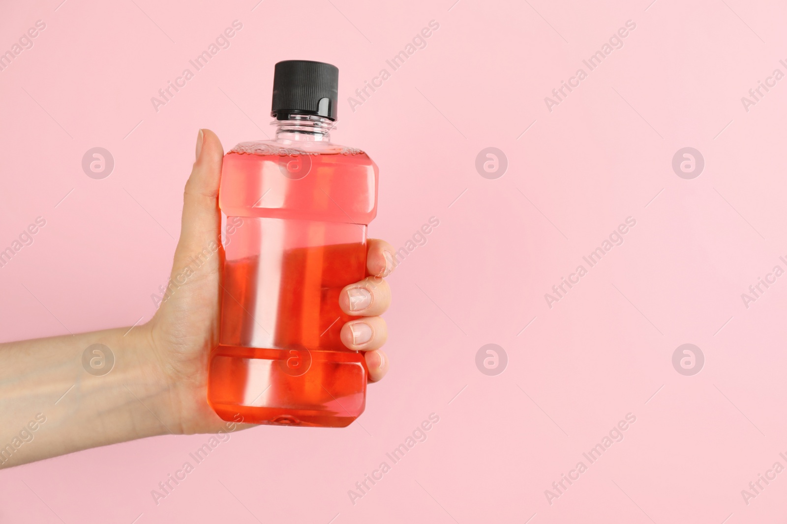 Photo of Woman holding bottle with mouthwash on pink background, closeup. Space for text