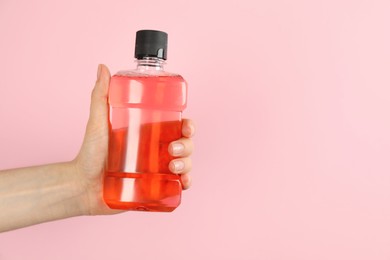 Photo of Woman holding bottle with mouthwash on pink background, closeup. Space for text