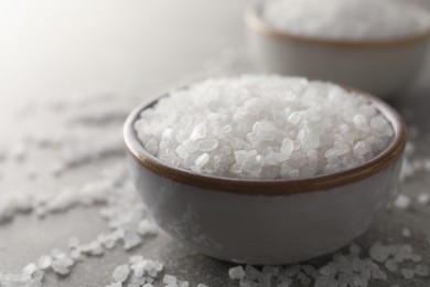 Photo of Bowls of natural sea salt on grey table, closeup