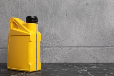 Photo of Motor oil in yellow canister on black table near grey wall, space for text