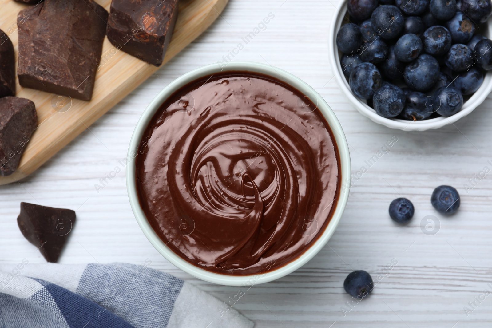 Photo of Delicious chocolate cream and blueberries on white wooden table, flat lay