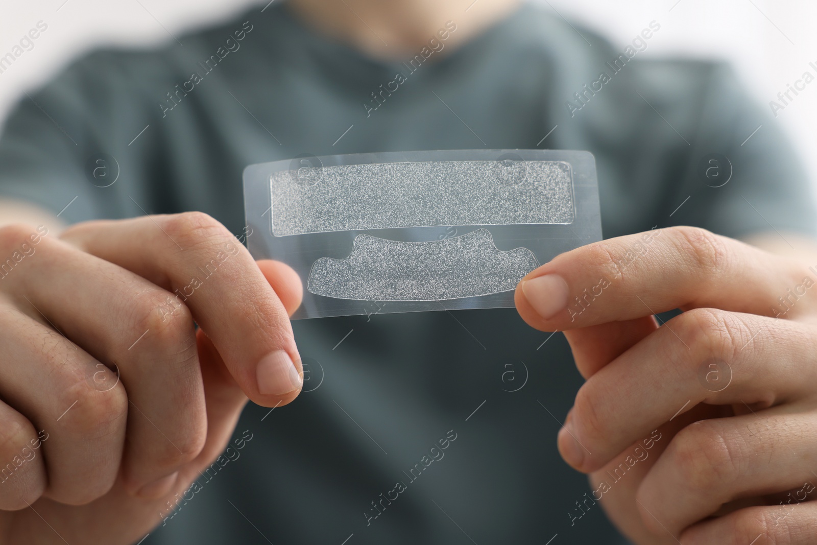 Photo of Young man with whitening strips, closeup of hands