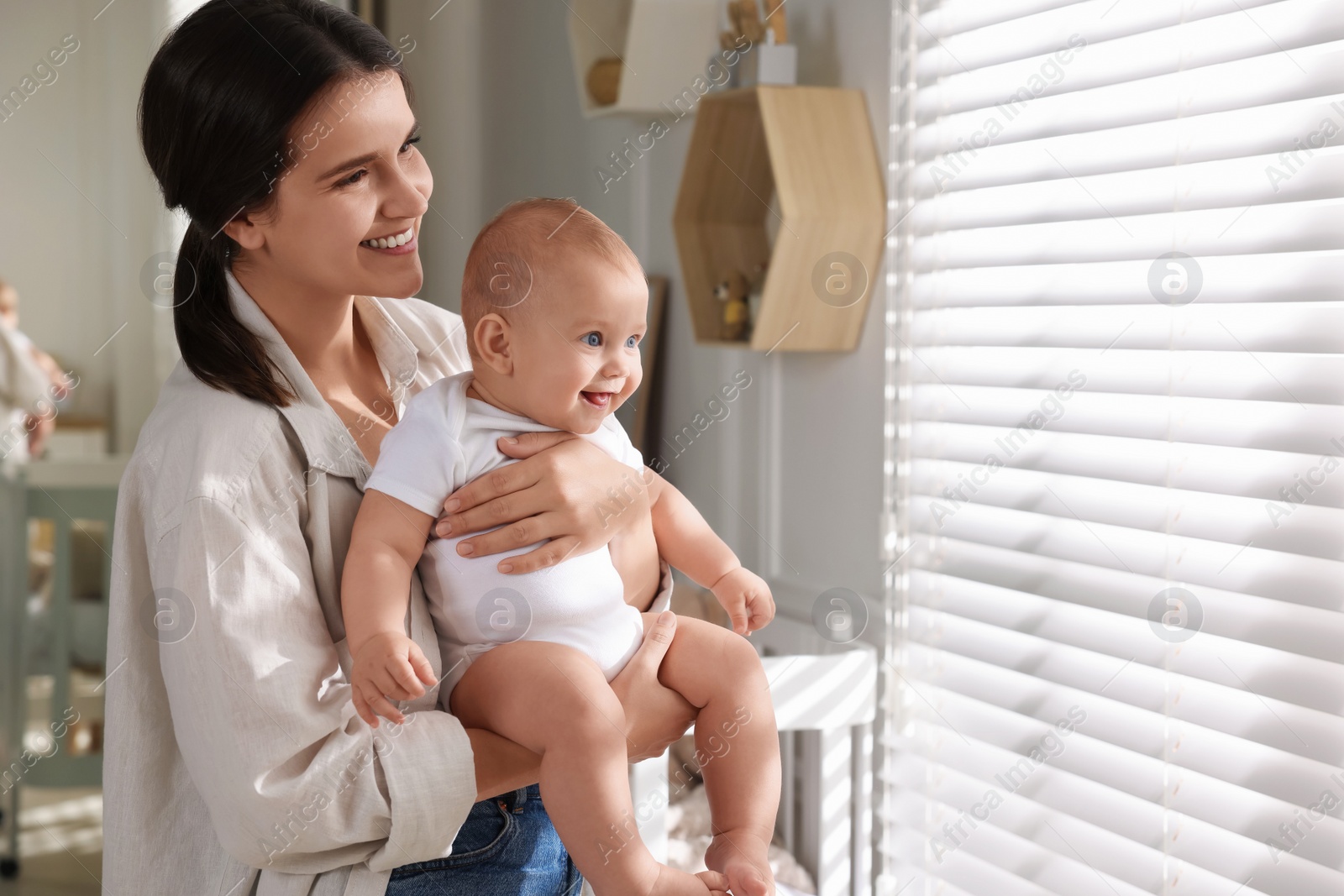 Photo of Happy young mother with her baby near window at home. Space for text