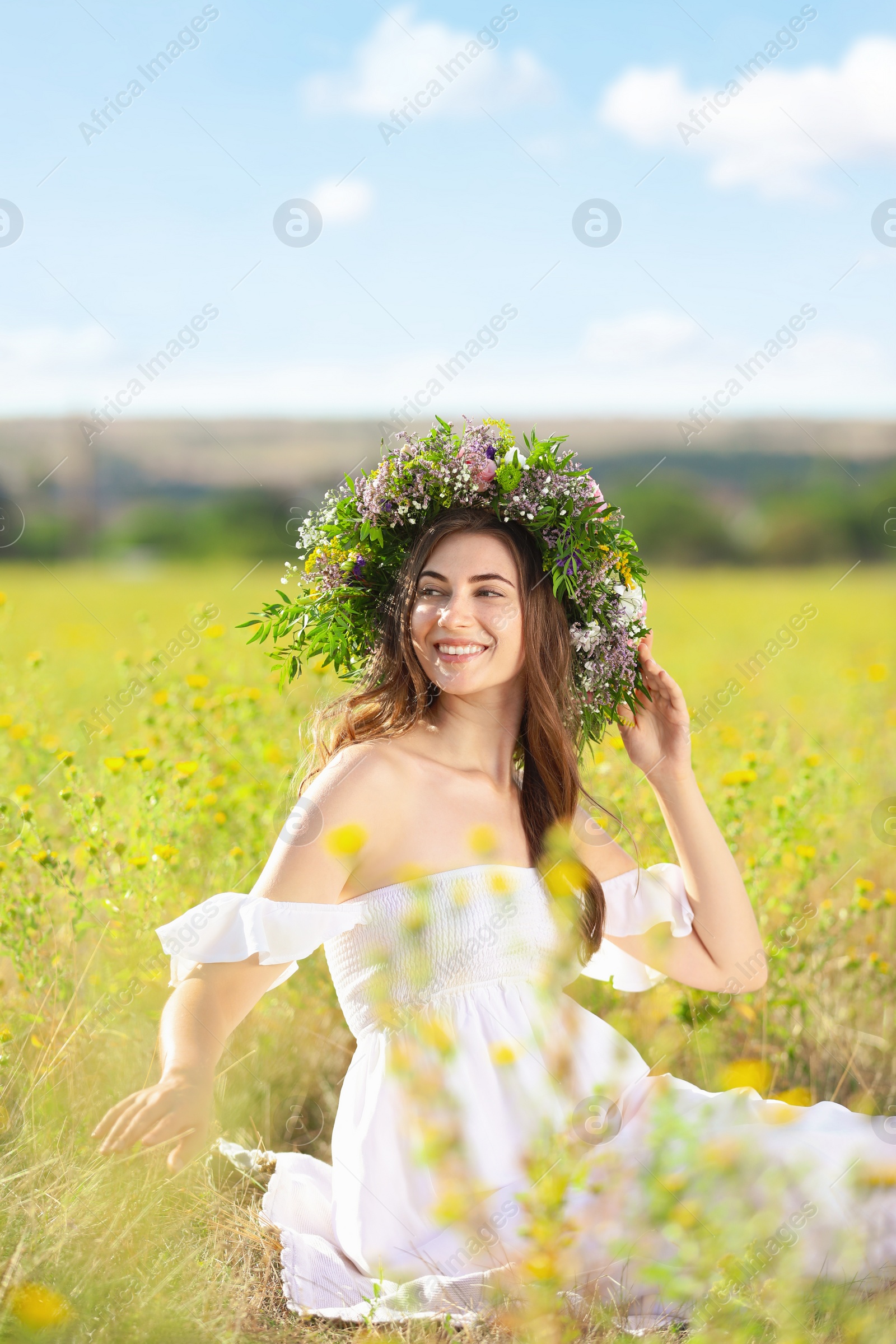 Photo of Young woman wearing wreath made of beautiful flowers in field on sunny day