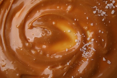 Photo of Delicious caramel sauce with sea salt as background, closeup