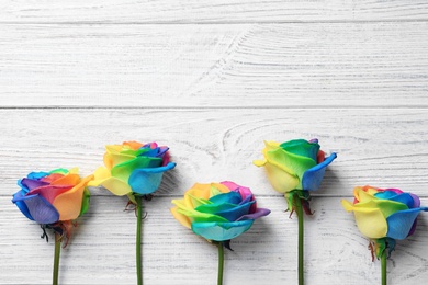 Photo of Rainbow rose flowers on wooden background, top view