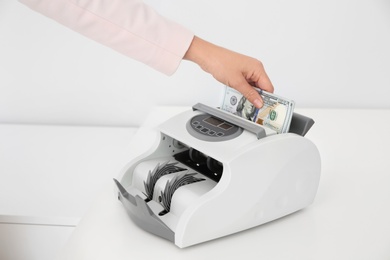 Photo of Woman putting money into counting machine on table, closeup