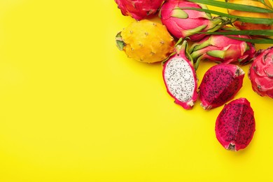 Photo of Different pitahaya fruits and palm leaf on yellow background, flat lay. Space for text