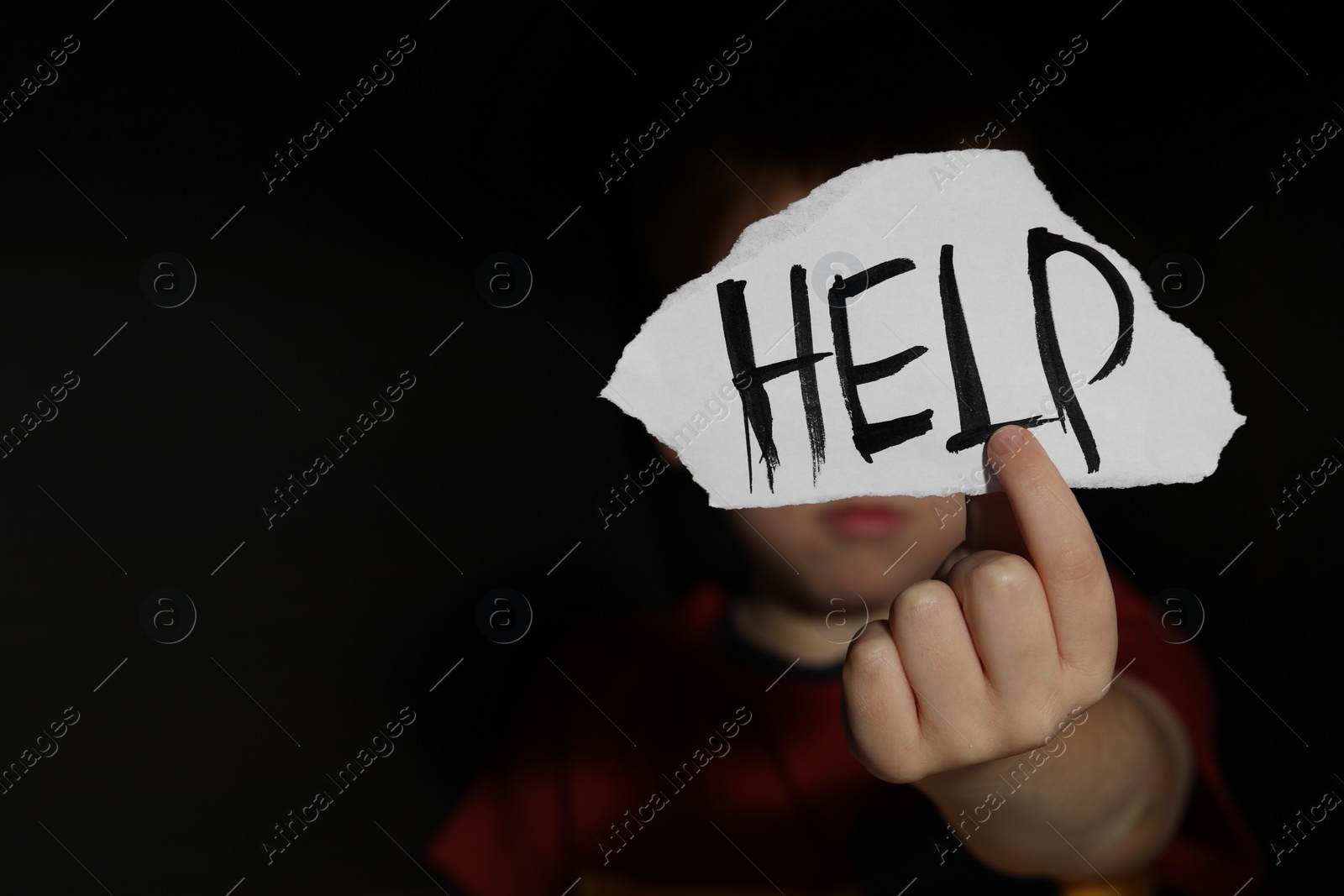 Photo of Little boy holding piece of paper with word Help on black background, space for text. Domestic violence concept