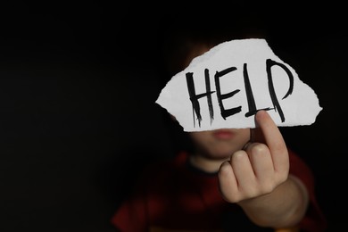 Photo of Little boy holding piecepaper with word Help on black background, space for text. Domestic violence concept