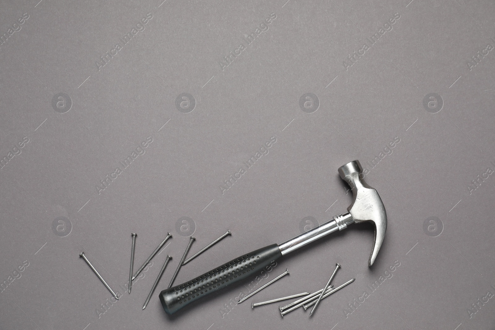 Photo of Hammer and metal nails on grey background, top view. Space for text