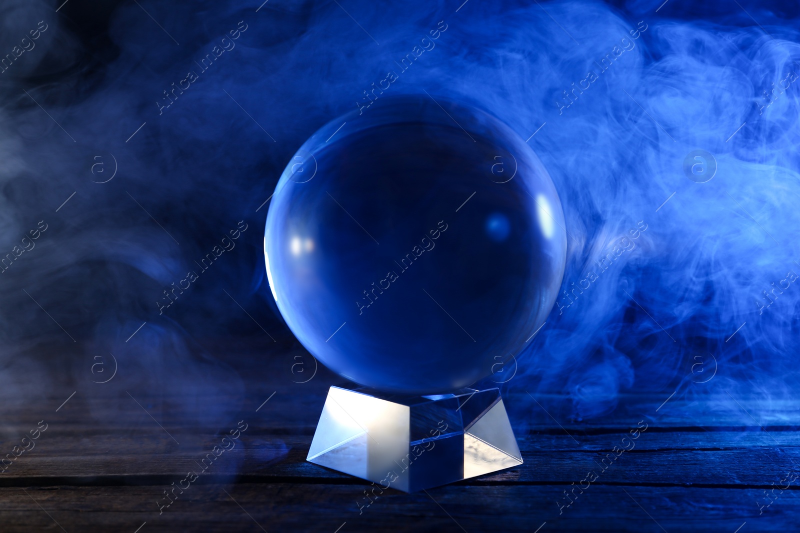 Photo of Magic crystal ball on wooden table and smoke against dark background. Making predictions