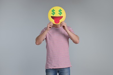 Photo of Man holding emoticon with dollar signs instead of eyes on grey background