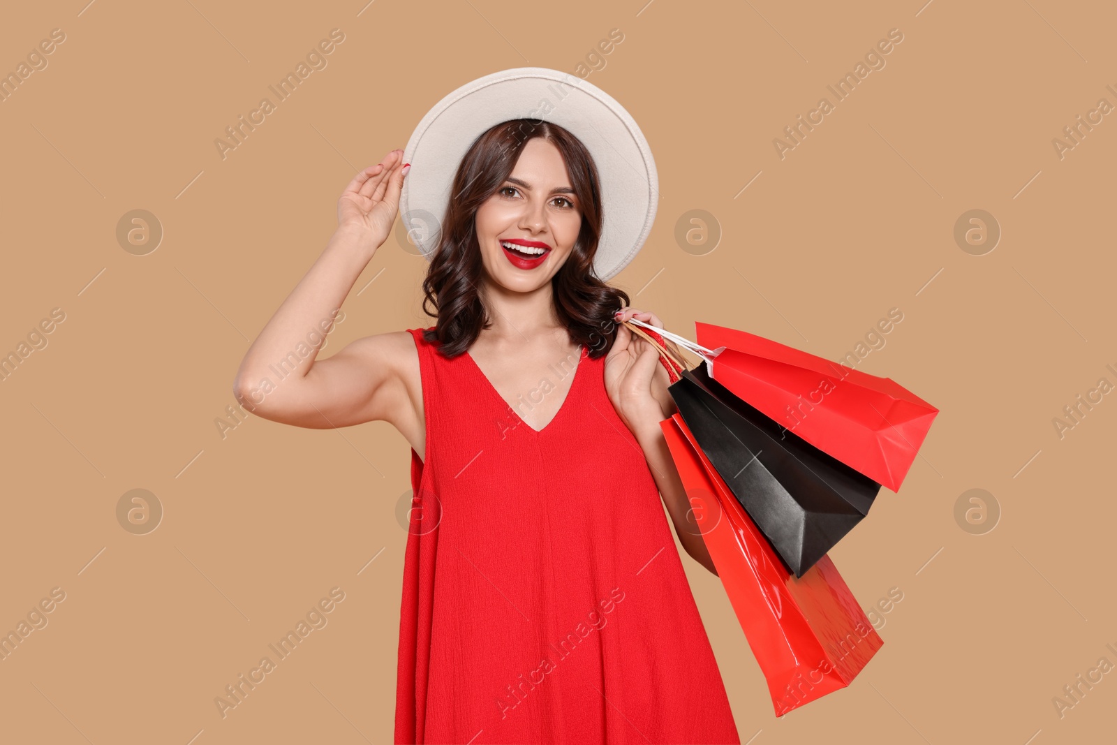 Photo of Beautiful young woman with paper shopping bags on beige background