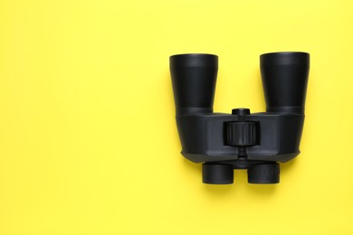 Modern binoculars on yellow background, top view. Space for text