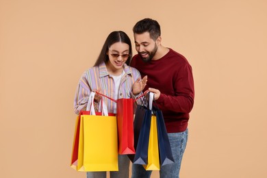 Man showing shopping bag with purchase to his girlfriend on beige background