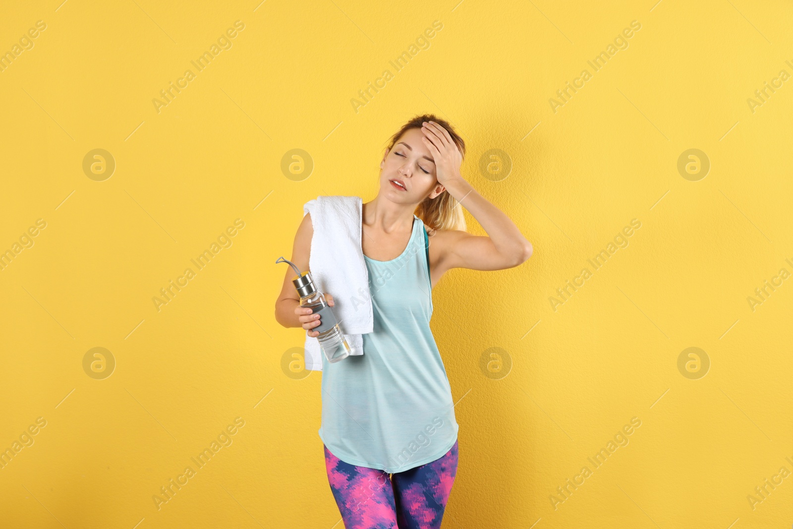 Photo of Beautiful young woman in sportswear with towel and bottle of water on color background