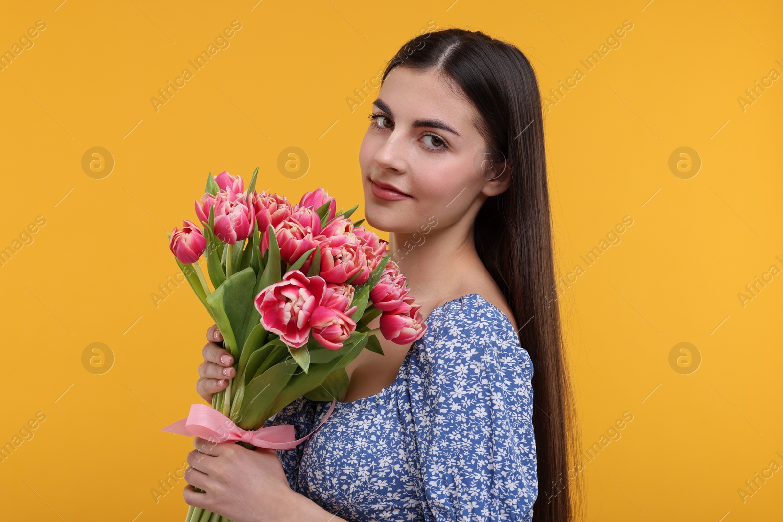 Photo of Happy young woman with beautiful bouquet on orange background