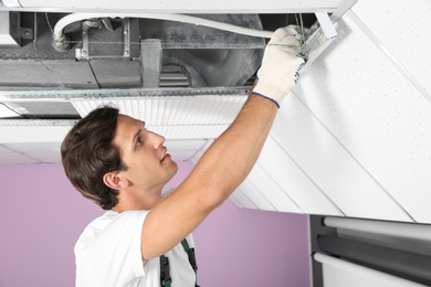 Photo of Young male technician repairing air conditioner indoors