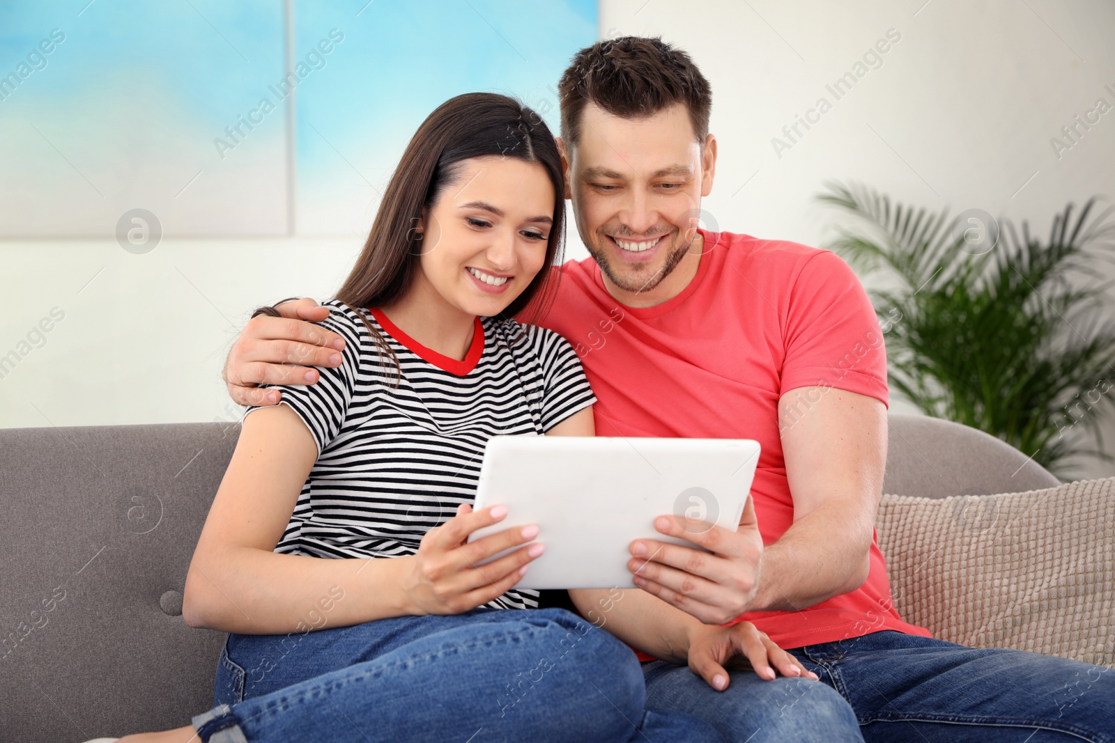 Photo of Happy couple with tablet sitting on couch at home