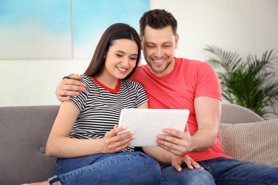 Happy couple with tablet sitting on couch at home