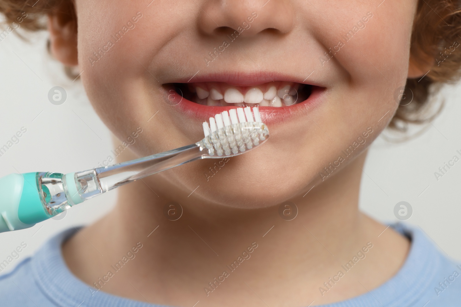 Photo of Cute little boy brushing his teeth with electric toothbrush on white background, closeup