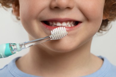 Cute little boy brushing his teeth with electric toothbrush on white background, closeup