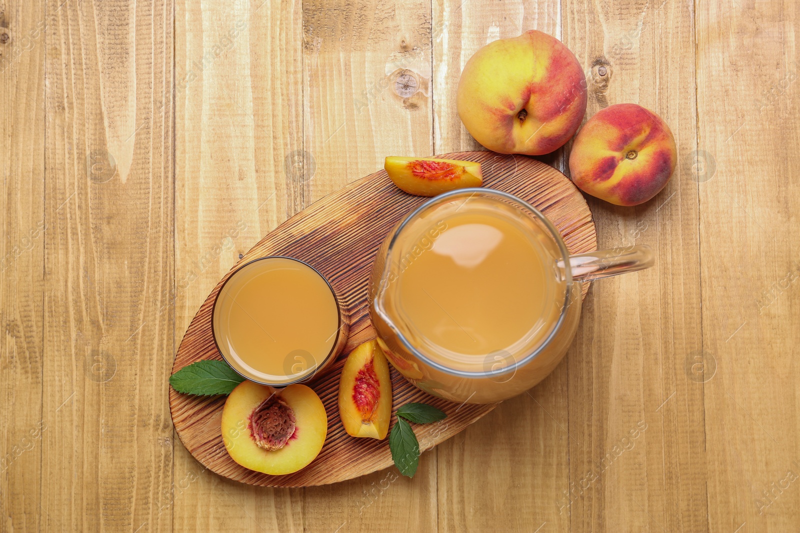 Photo of Delicious peach juice, fresh fruits and leaves on wooden table, flat lay