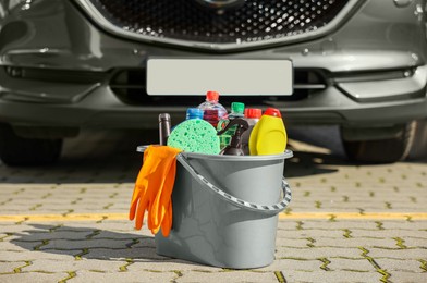 Car cleaning products in bucket near automobile outdoors on sunny day