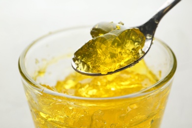 Photo of Spoon with fruit jelly over glass on light background, closeup