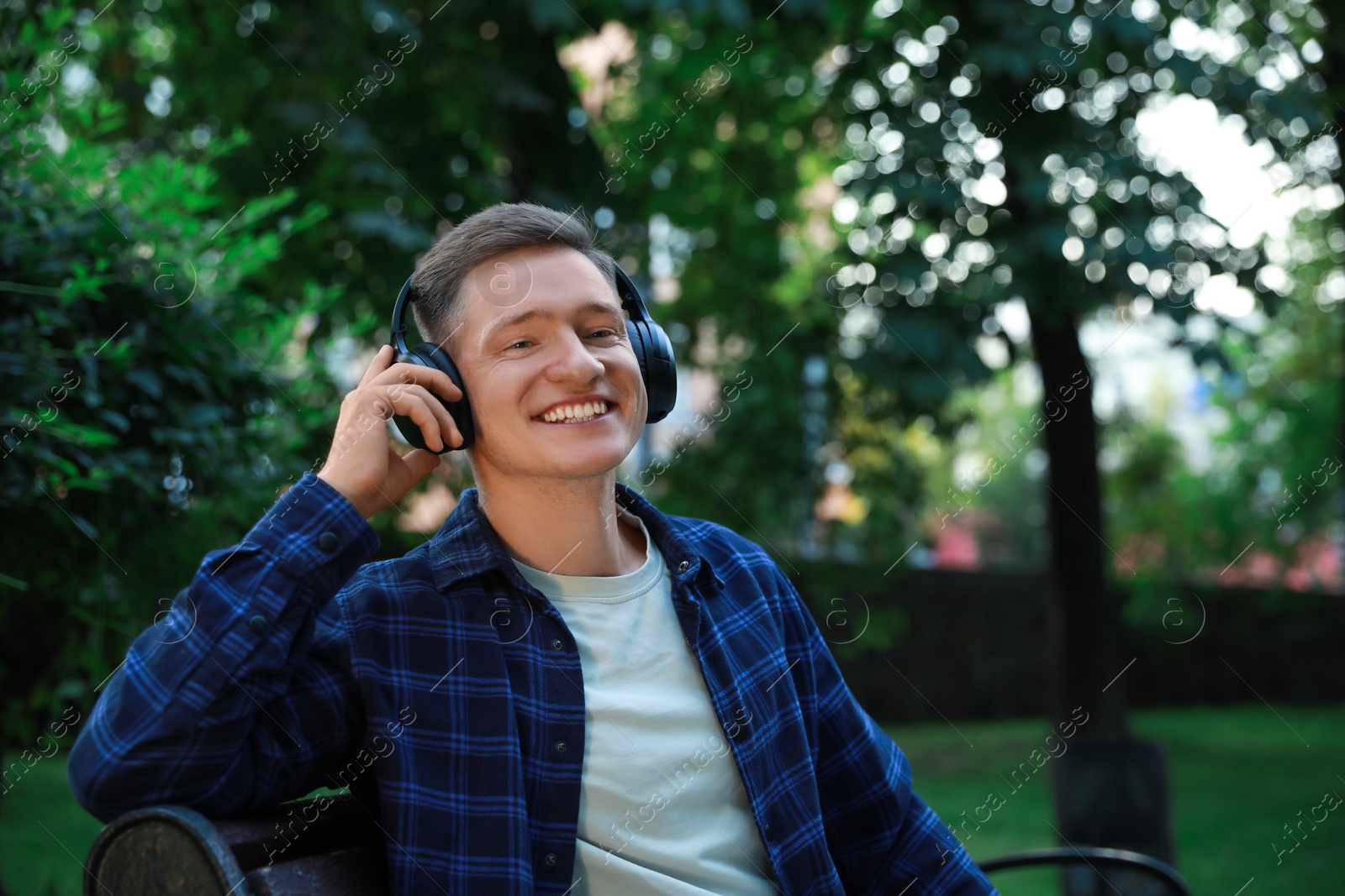 Photo of Smiling man in headphones enjoying music in park. Space for text