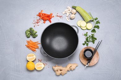 Photo of Wok, chopsticks and different products on grey table, flat lay