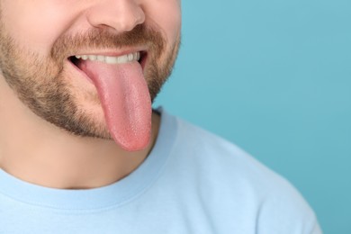 Image of Man showing long tongue on light blue background, closeup