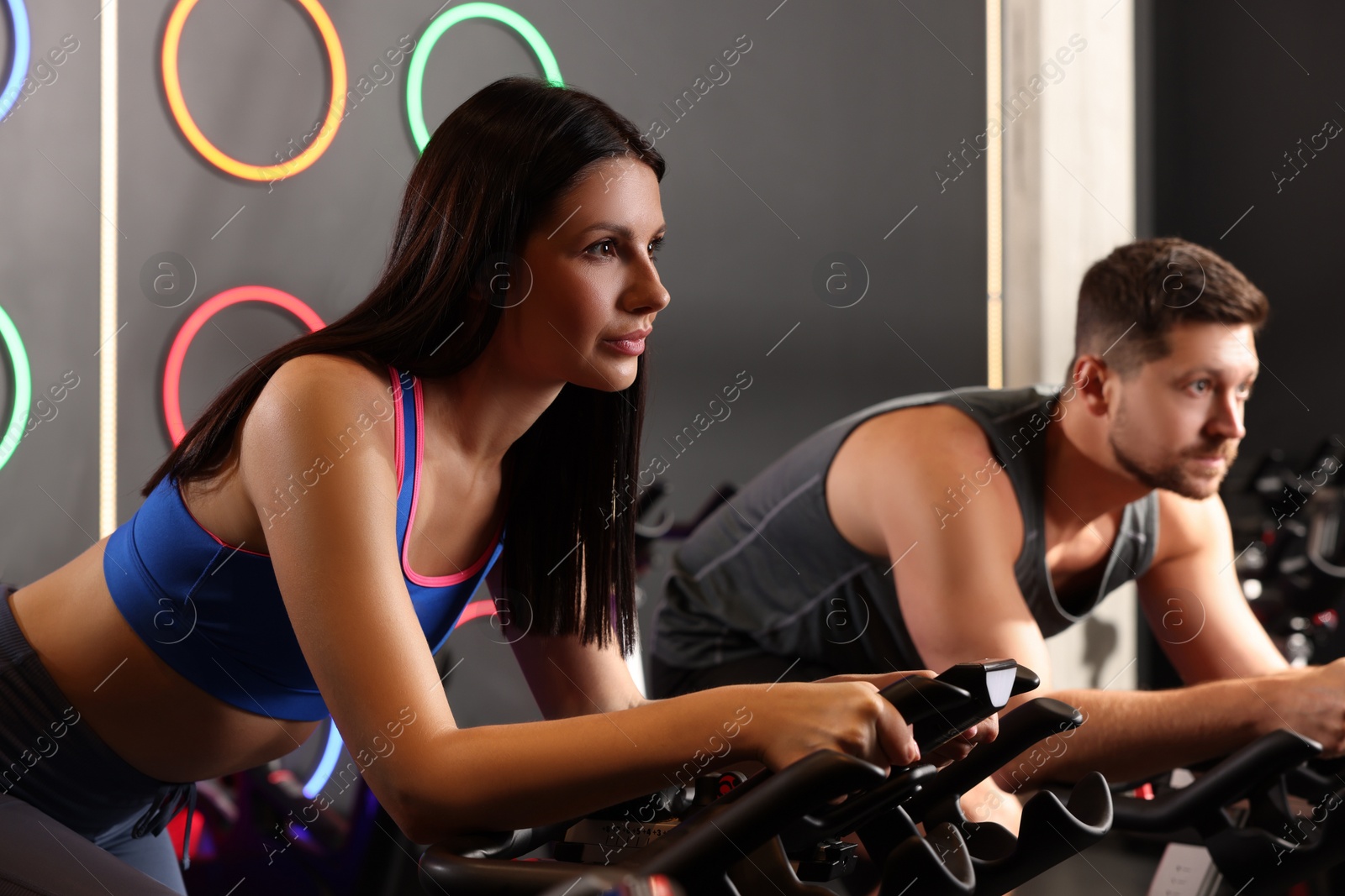 Photo of Young woman and man training on exercise bikes in fitness club