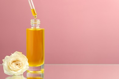 Photo of Dripping face serum into bottle on pink background. Space for text