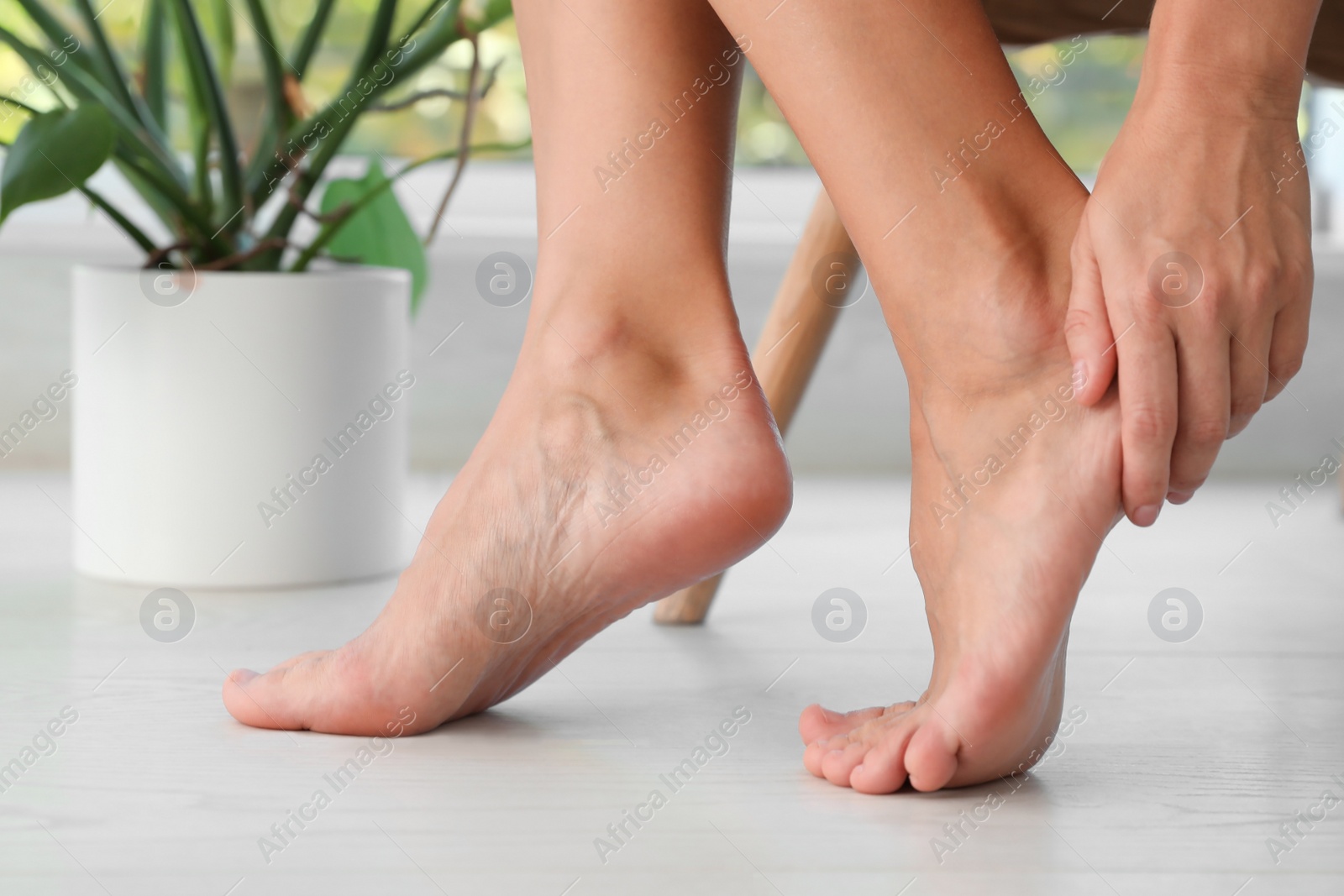 Photo of Woman suffering from foot pain at home, closeup